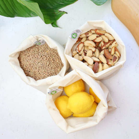 3 Reusable produce bags made with organic cotton, filled with lentils, lemons, and nuts for a plastic-free, eco-friendly shopping solution