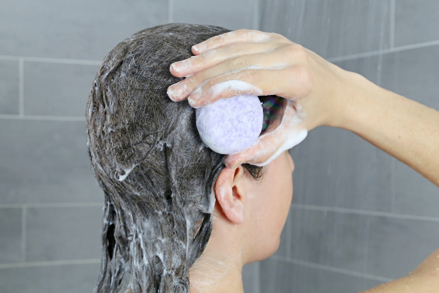 woman using a natural and vegan shampoo bar made of lavender in her head, making some lather in the shower, from beewise amsterdam brand
