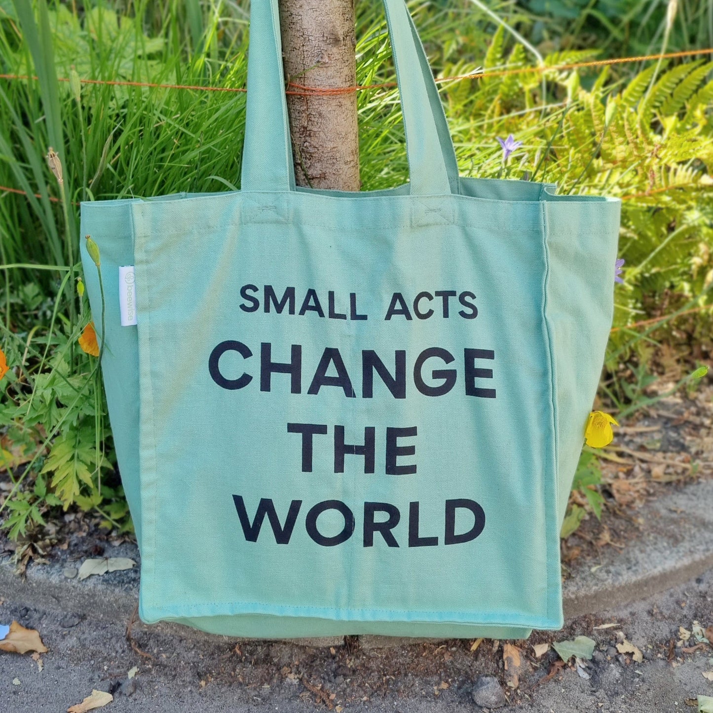 grocery bag multi pocket with 6 sleeves inside made of organic green cotton with the sentence: small acts change the world hanging on a wood stick