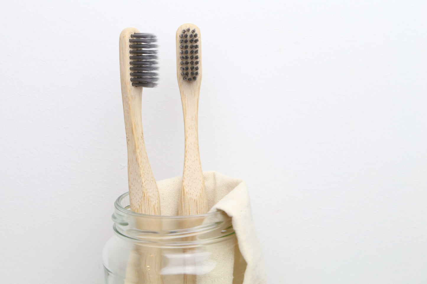 Two bamboo toothbrushes for adults from beewise soft charcoal bristles inside a glass container in the bathroom
