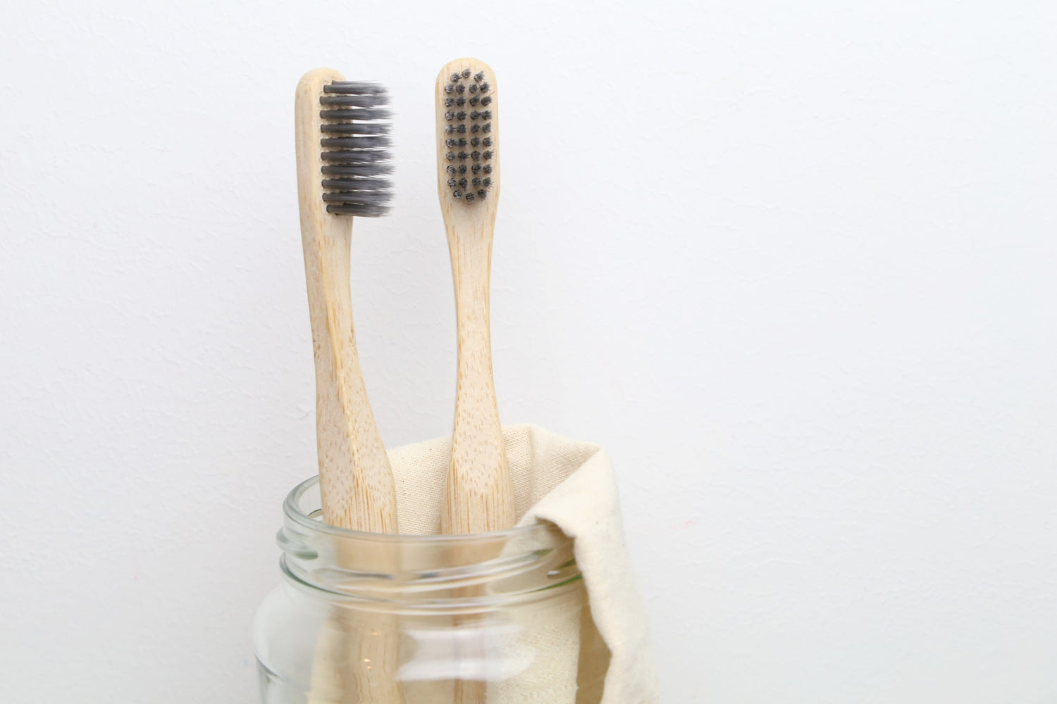 Two bamboo toothbrushes for adults from beewise soft charcoal bristles inside a glass container in the bathroom