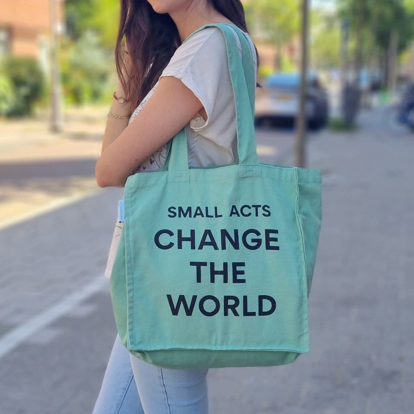 sustainable & plastic-free reusable grocery bag with multiple pockets and 6 sleeves inside, made of organic green cotton, featuring the phrase "Small acts change the world" and being used by a girl. The design emphasizes sustainability and eco-friendliness