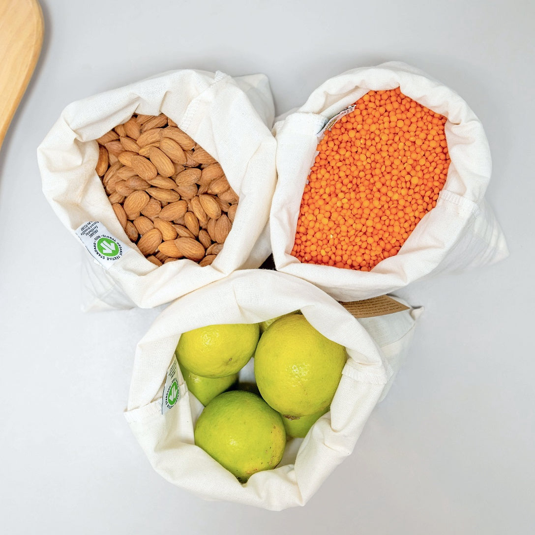 3 Reusable produce bags made with organic cotton, filled with lentils, lemons, and nuts for a plastic-free, eco-friendly shopping solution