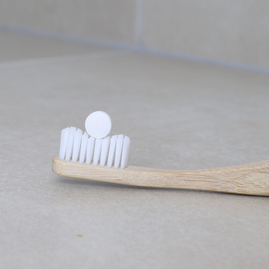 zero waste & sustainable toothpaste tablet on top of a white bristles bamboo toothbrush