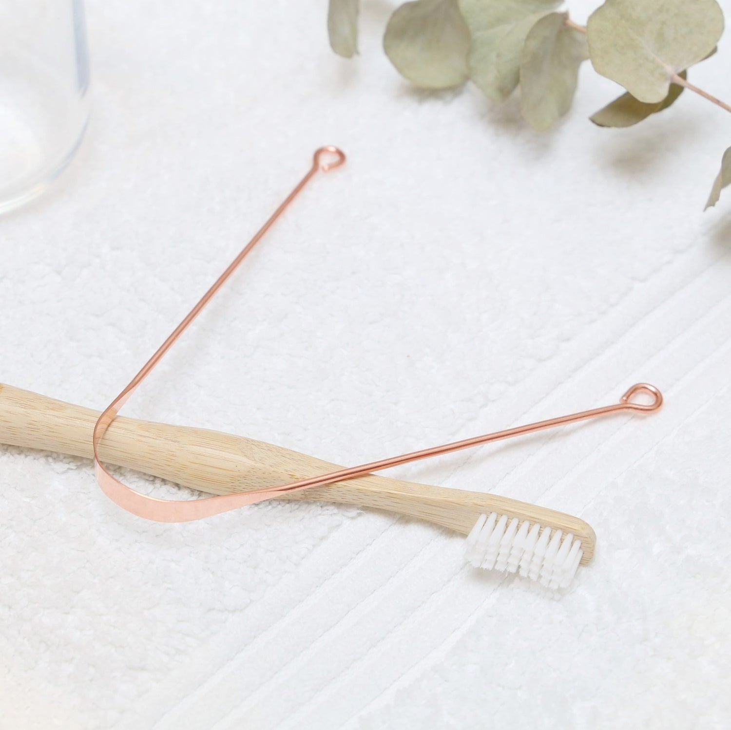metal tongue cleaner made in copper on top of a bamboo toothbrush