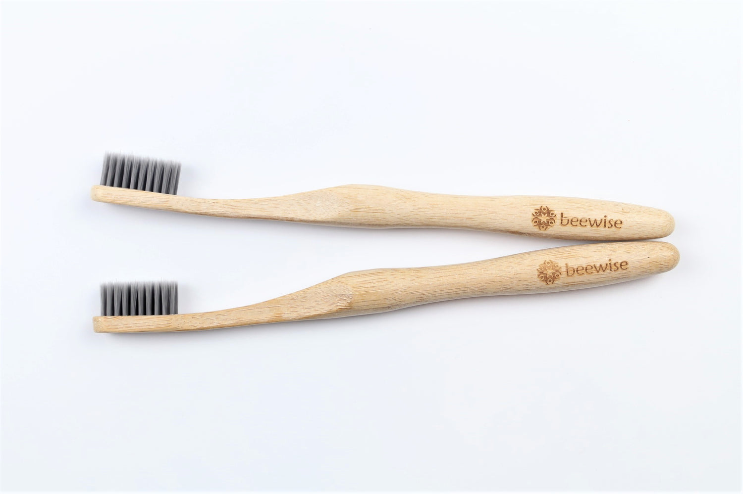 Two bamboo toothbrushes for adults from beewise soft charcoal bristles on the sink of a bathroom.