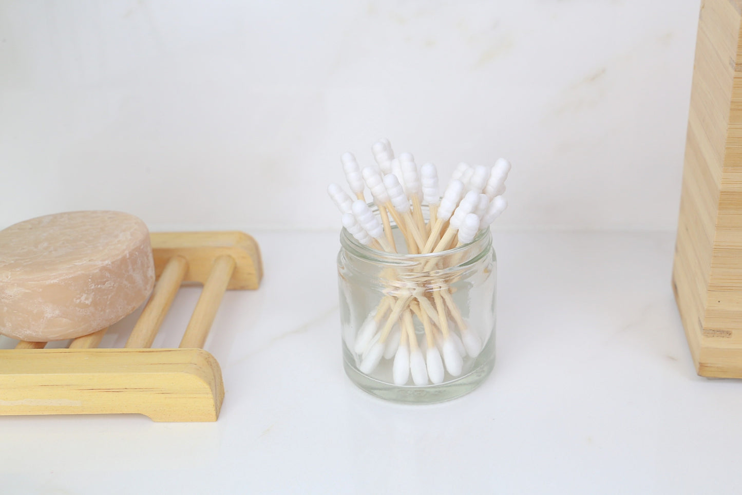 bamboo cotton buds home compostable inside a glass container from beewise on top of the bathroom sink next to a soap bar