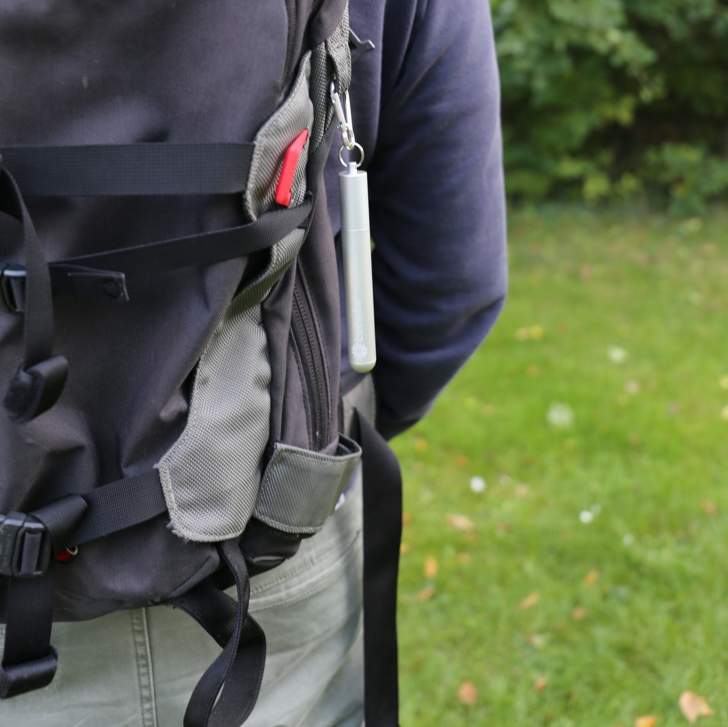 reusable straw collapsible silver case and silver colour being used attached to a backpack of a man