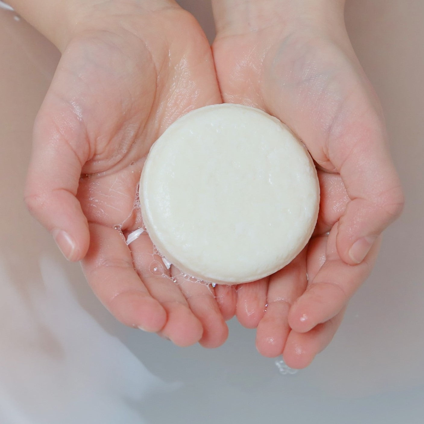 sustainable and eco-friendly shampoo rounded bar for baby and kids on the hands of a child with some bubbles