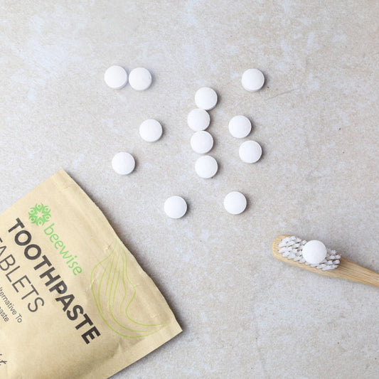 sustainable & vegan toothpaste tablet in a white bristles bamboo toothbrush with a kraft packaging and some toothtablets spread